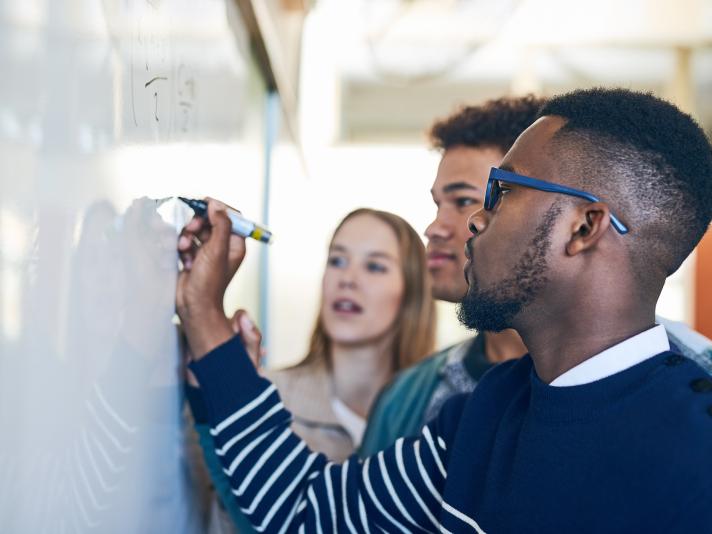 Shot of a young man writing on a whiteboard while students look on